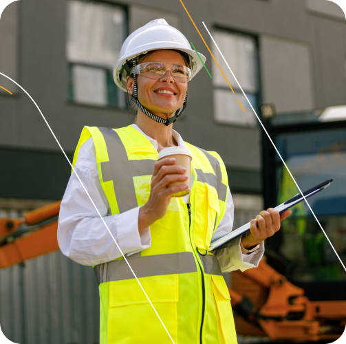 Smiling construction worker in a safety vest and helmet holding a coffee cup and clipboard on a job site