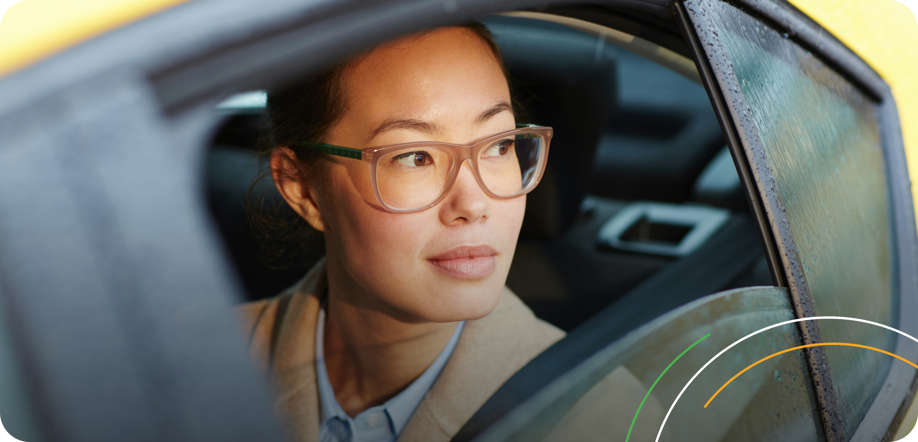A woman with glasses looking out of a wet car window.