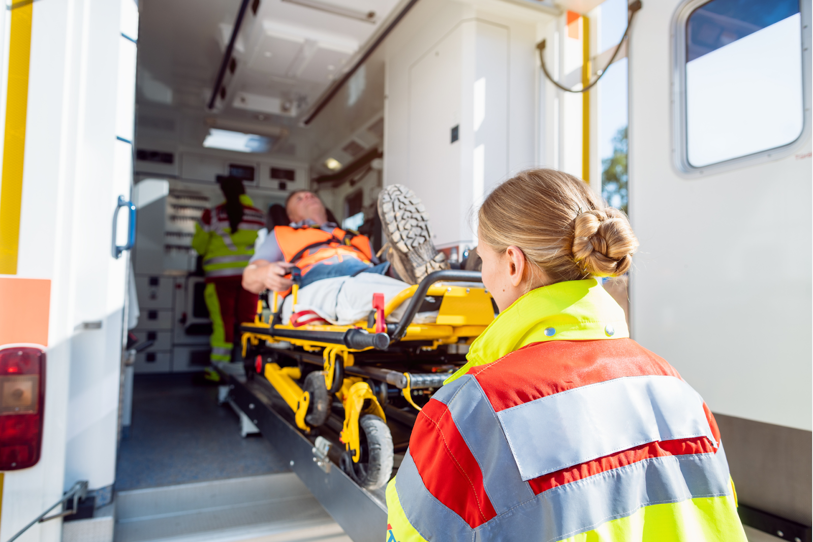 A female paramedic assists in loading a patient into an ambulance.