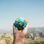 An open palm is pictured holding a ball of the Earth against a backdrop of mountains.
