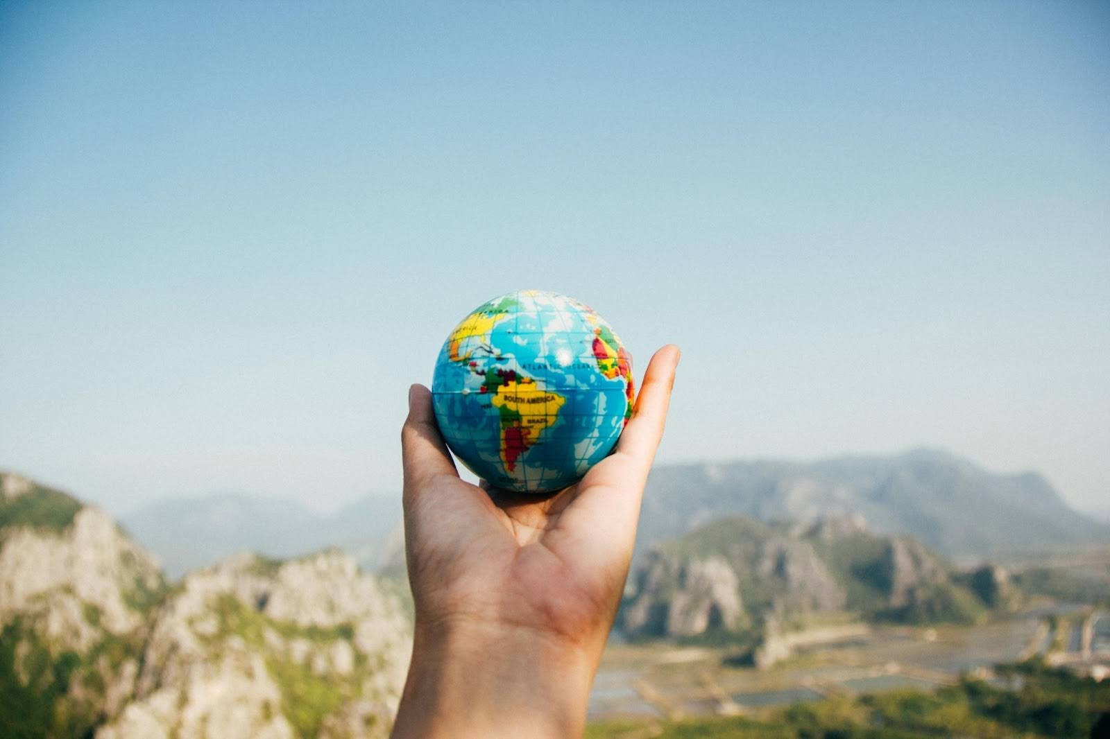 An open palm is pictured holding a ball of the Earth against a backdrop of mountains.
