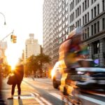 A busy intersection with blurred bicyclists, pedestrians, and cars showing rapid movement.