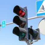 A red traffic light controls traffic where cars, pedestrians, and bicycles meet.