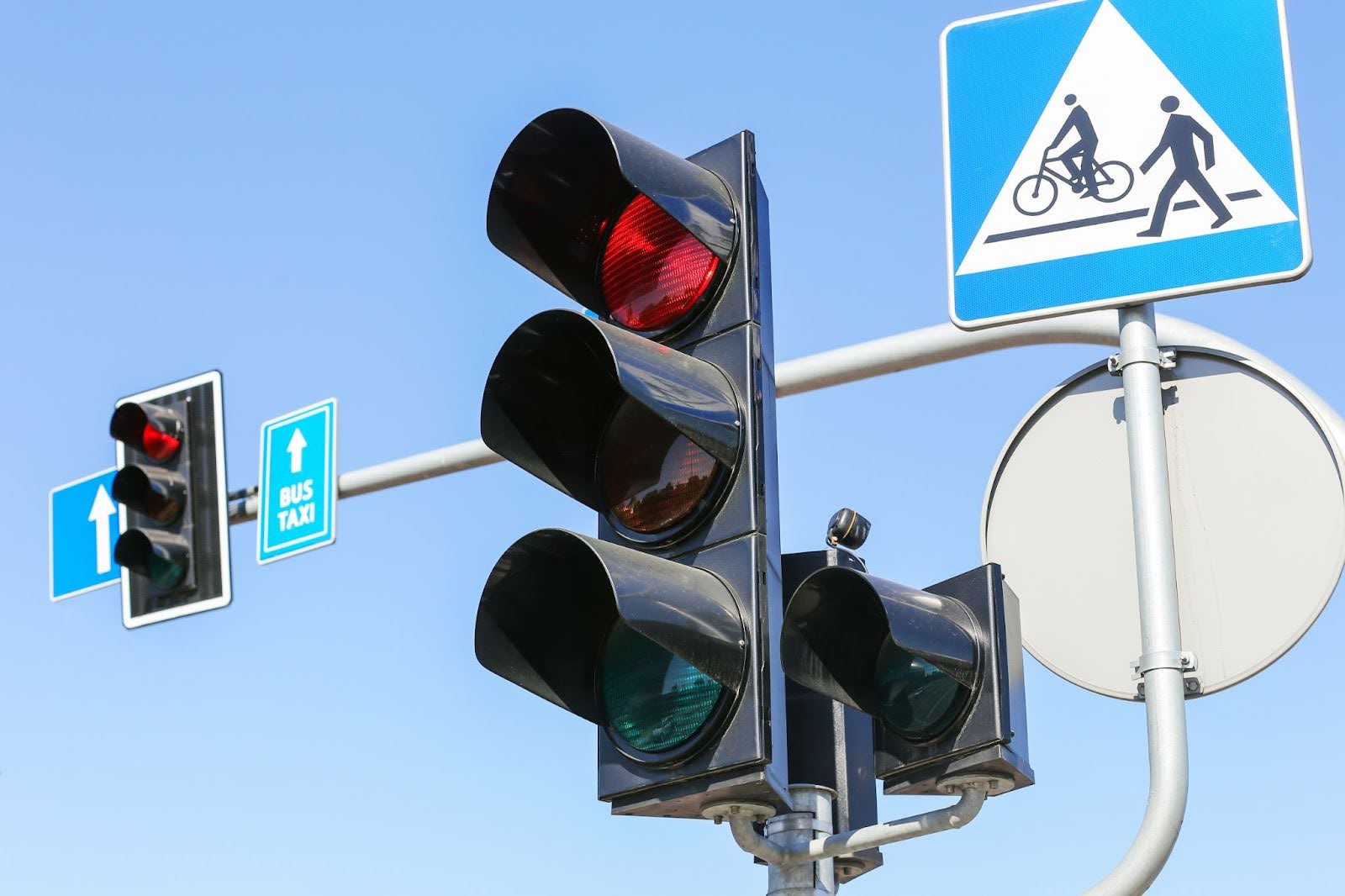 A red traffic light controls traffic where cars, pedestrians, and bicycles meet.