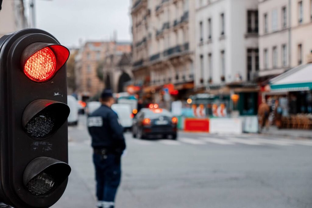 A vintage black traffic light with the red light on, a cop at an intersection behind blurred out