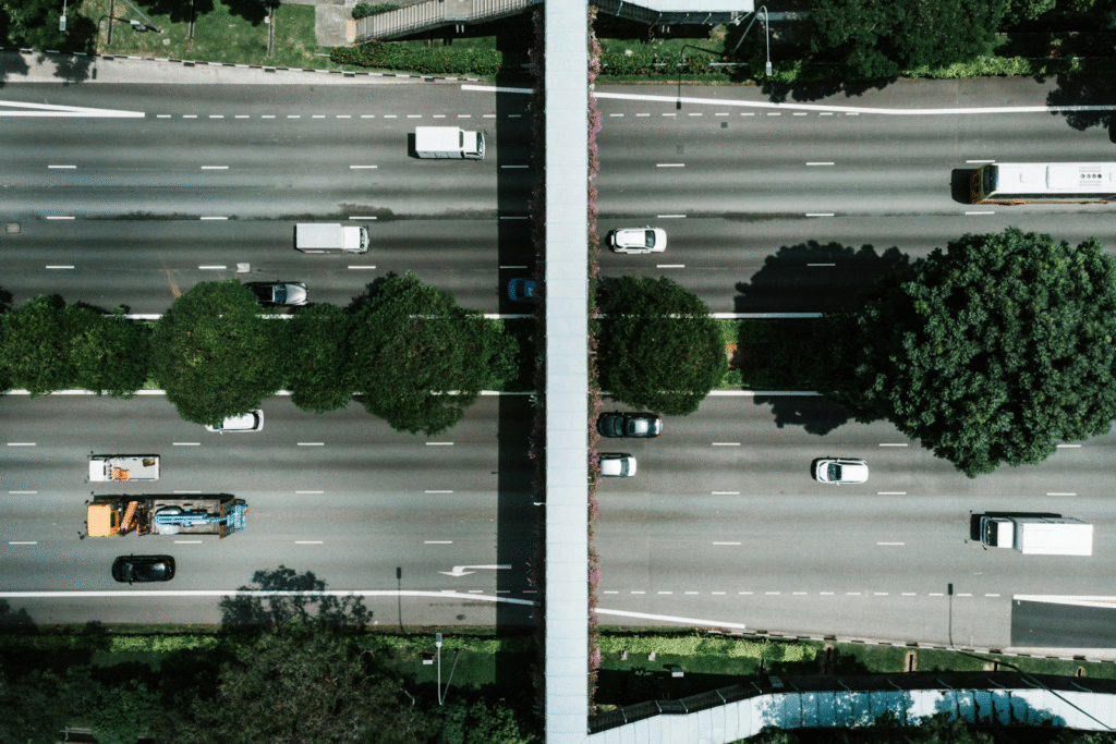 Aerial shot of multi-line highway with an overpass, tree median, and a few vehicles. 
