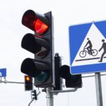 A black traffic light with the red light on, surrounded by other pedestrian and traffic signs