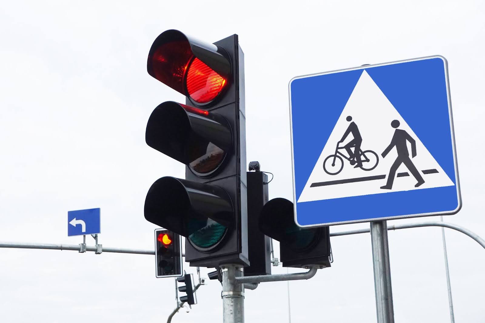 A black traffic light with the red light on, surrounded by other pedestrian and traffic signs