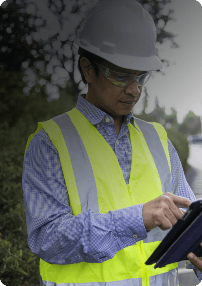 Traffic engineer in a hard hat and safety vest reviewing data on a tablet at the roadside